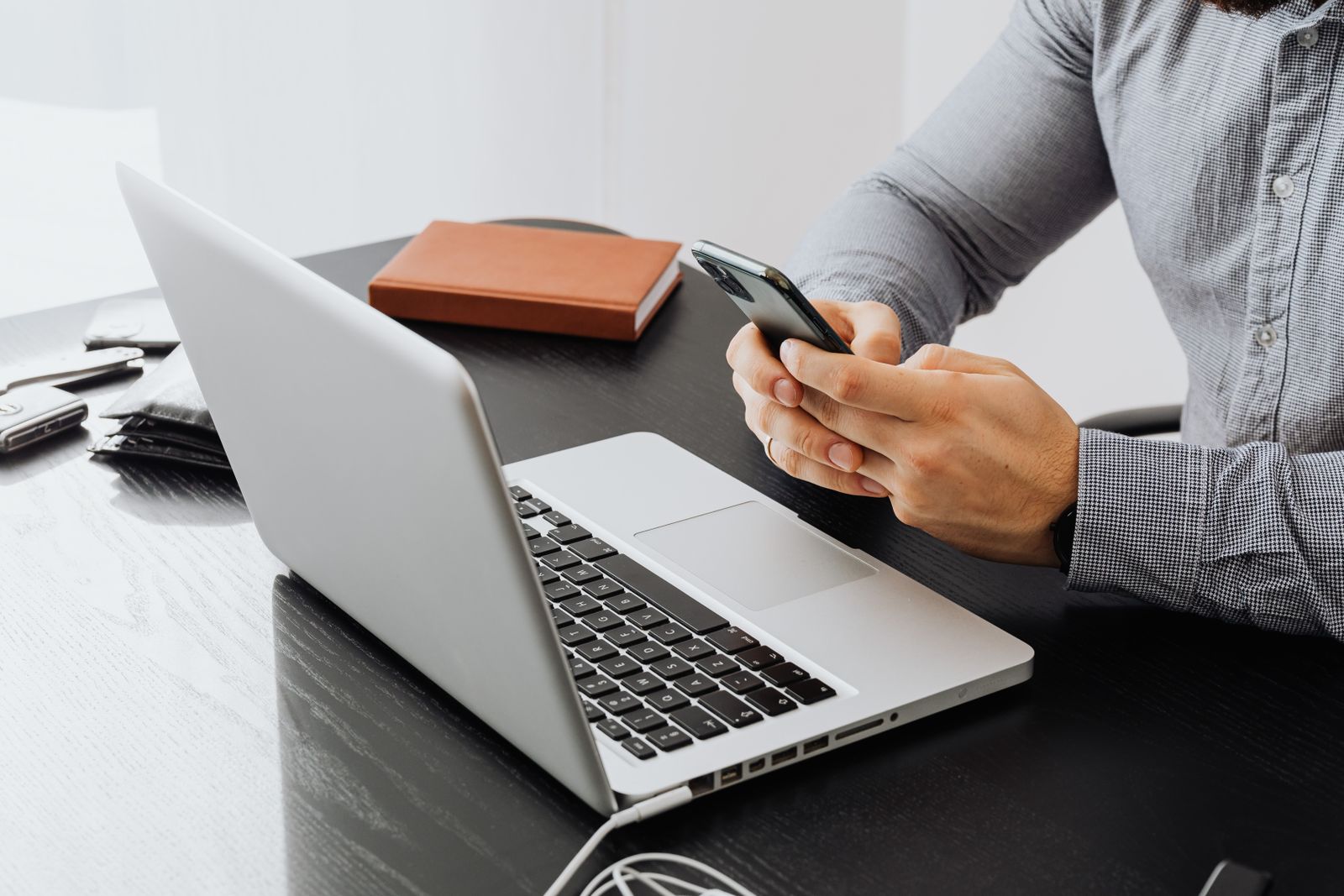 Persona con camisa gris usando su teléfono frente a una laptop en un escritorio