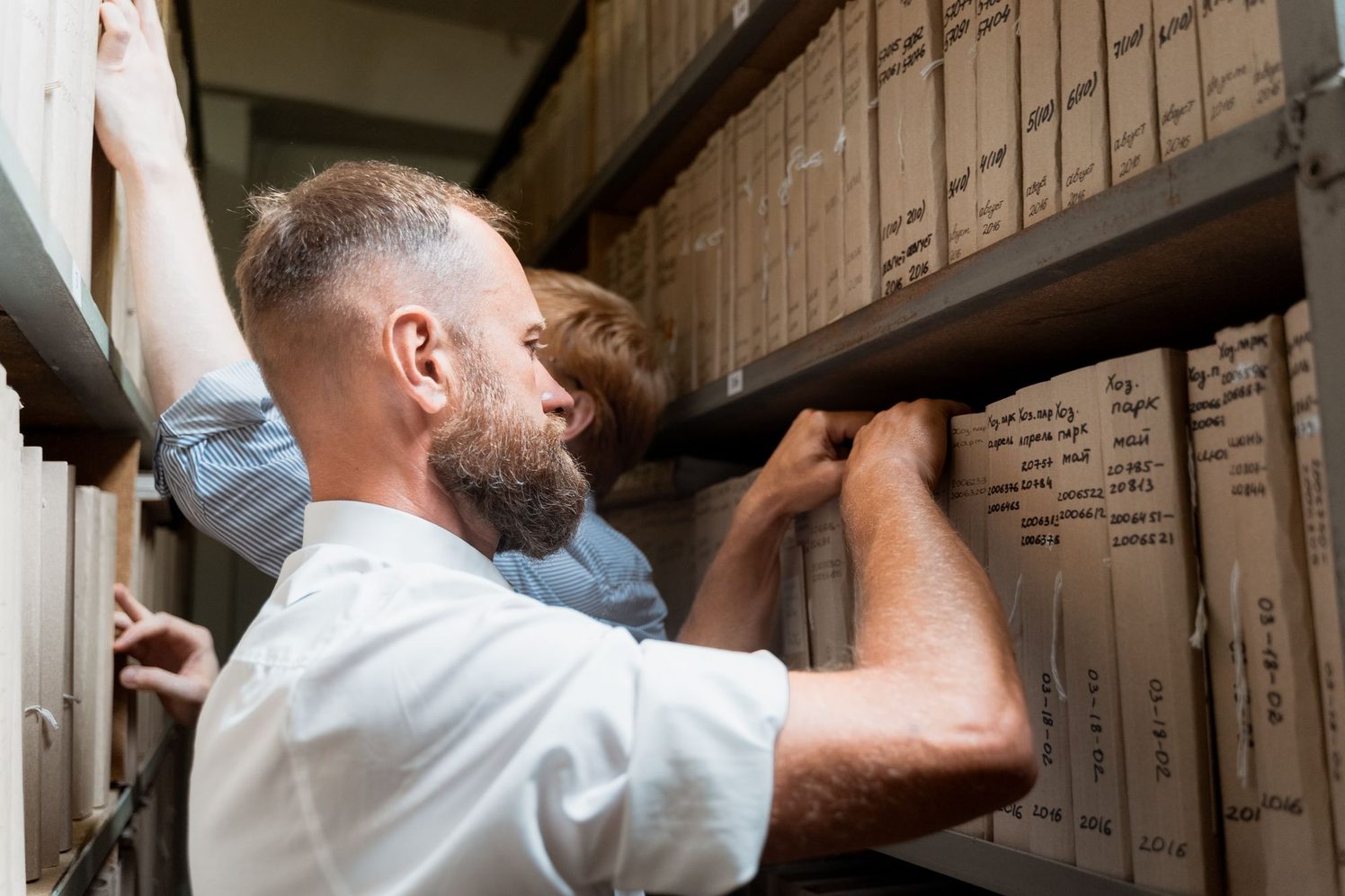 Dos personas buscan un documento entre archivadores en un archivo