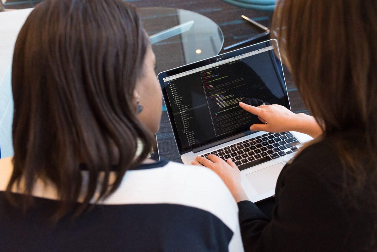Dos profesionales revisan el código de un sistema en una laptop