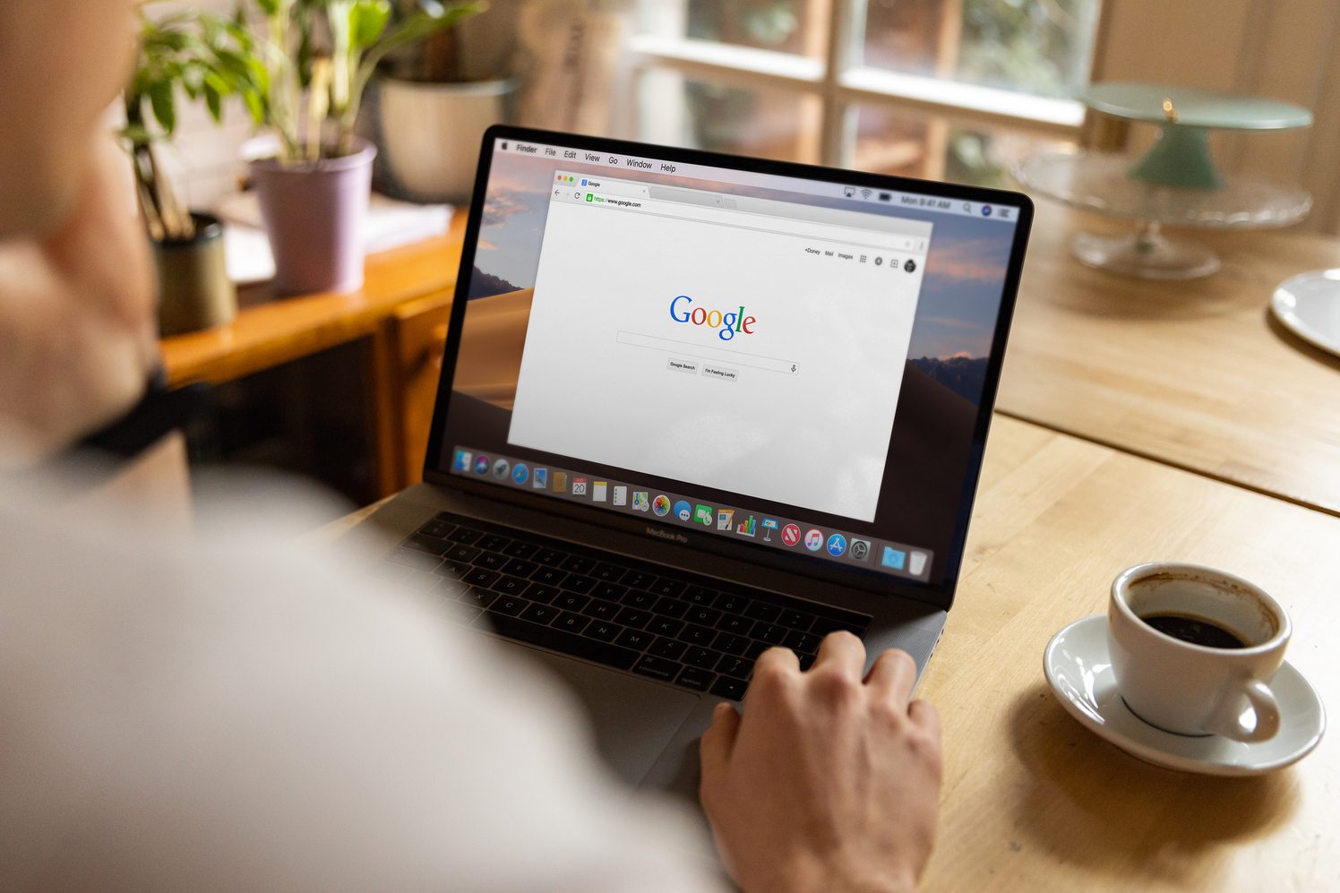 Persona frente a una laptop con la página de inicio de Google abierta, con una taza de café al lado