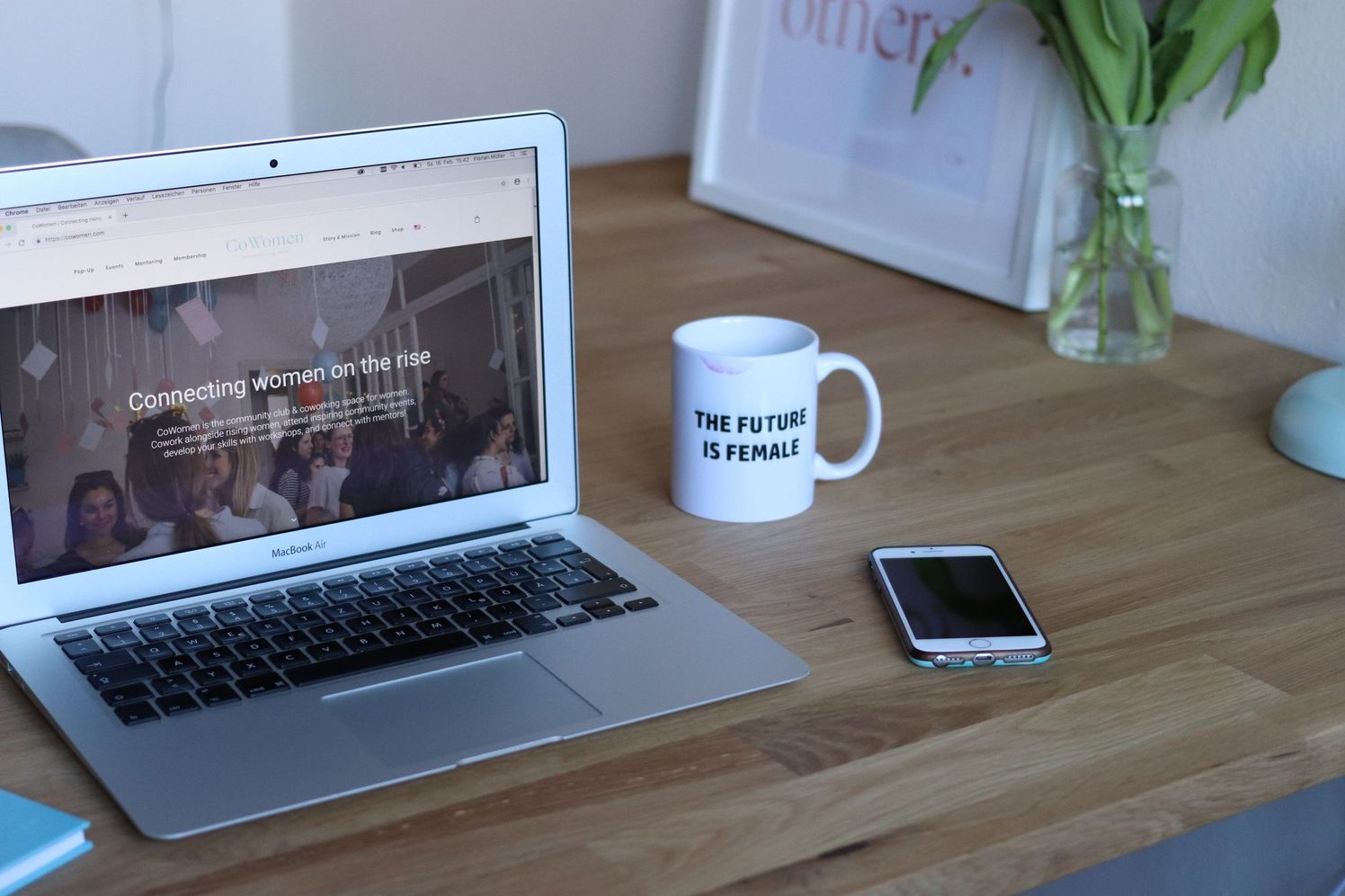 Laptop con un sitio web abierto junto a un celular y una taza sobre un escritorio de madera